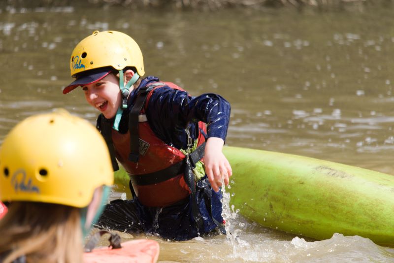 A picture of a scout climbing out of the water after having capsized while kayaking